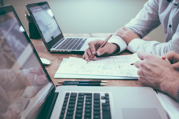 Zwei Personen sitzen am Tisch mit Laptops und Unterlagen 