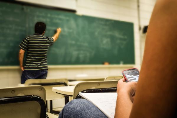 Klassenzimmer mit Lehrer an der Tafel und Schüler mit Handy