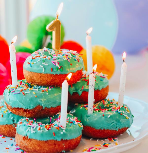 gestapelte Muffins mit bunter Glasur, Kerze in Form der Zahl 1 und Luftabllons im Hintergrund